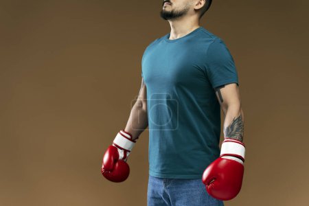 Foto de Retrato de hombre con guantes de boxeo rojos haciendo ejercicios aislados sobre fondo marrón. Guapo barbudo entrenamiento masculino, moviéndose, teniendo hobby - Imagen libre de derechos