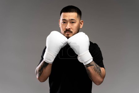 Téléchargez les photos : Boxer coréen en gants de boxe blancs s'entraînant isolé sur fond gris. Jeune homme attrayant faisant du sport, de la motivation, un mode de vie sain concept - en image libre de droit