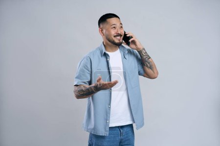 Photo for Handsome asian man with brunette hair talking smartphone approving order calling friend at studio alone. Technology and people concept - Royalty Free Image