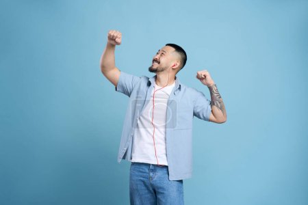 Foto de Alegre hombre asiático feliz usando auriculares escuchando música aislada sobre fondo azul, espacio de copia. Tecnología, concepto de emociones positivas - Imagen libre de derechos