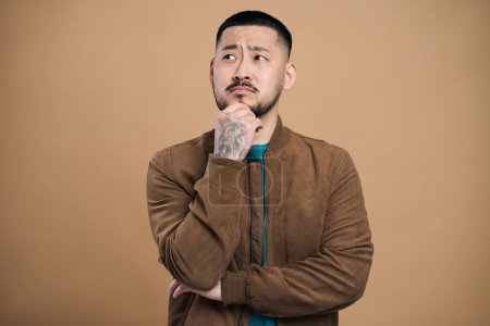Photo for Portrait of bearded asian thoughtful man in casual style clothes thinking and looking distance. Studio shot on brown background - Royalty Free Image