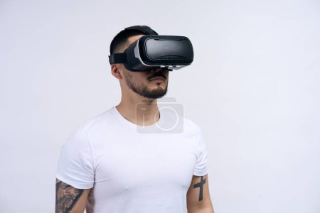 Photo for Young man wearing white shirt using virtual reality headset isolated on white background studio. VR, future, gadgets, technology, education online, studying, video game concept - Royalty Free Image