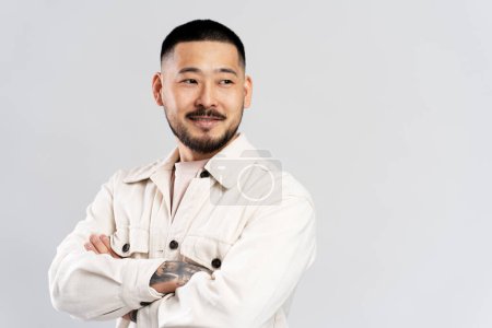 Téléchargez les photos : Portrait de bel homme asiatique élégant aux cheveux élégants, portant des vêtements décontractés, les bras croisés regardant loin, isolé sur fond blanc. Espace de copie - en image libre de droit