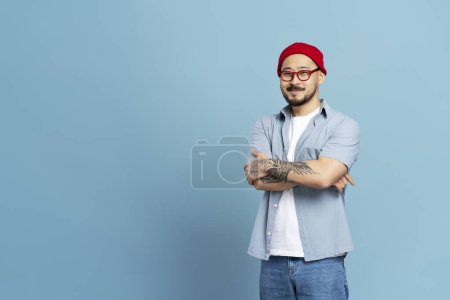 Photo for Smiling asian man with arms crossed and stylish tattoo isolated on blue background, copy space - Royalty Free Image