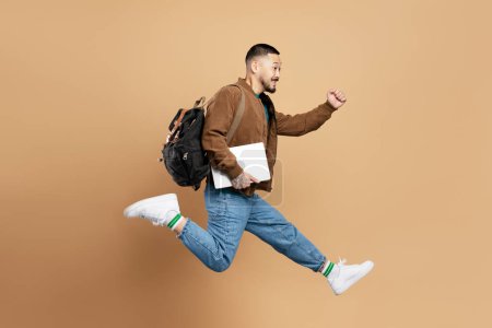 Photo for Portrait of busy emotional asian student with backpack, holding laptop, running fast, hurry up to university isolated on beige background. Education concept - Royalty Free Image