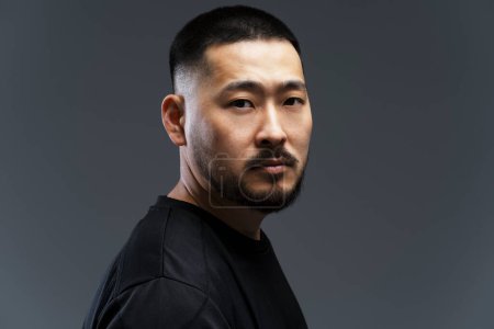Photo for Dramatic portrait of handsome serious asian man with stylish hair, beard looking at camera, isolated on black background - Royalty Free Image