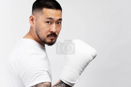 Téléchargez les photos : Portrait d'un bel homme asiatique sérieux, boxeur portant des gants de boxe blancs regardant la caméra, isolé sur fond. Sport, mode de vie sain concept - en image libre de droit