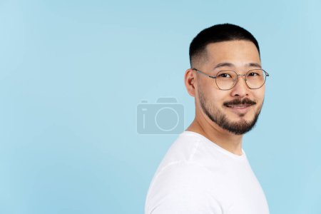 Photo for Portrait of handsome smiling asian man wearing stylish eyeglasses, white t shirt isolated on blue background. Happy successful Korean student looking at camera, copy space. Education concept - Royalty Free Image