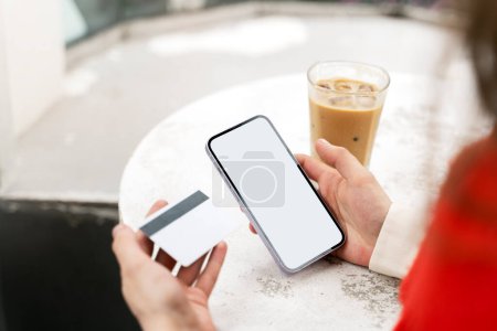 Foto de Concepto de compras en línea, compras por Internet. Mujer usando smartphone, con tarjeta bancaria en la mano, tomando café en la cafetería, primer plano. Pantalla blanca, espacio para anuncios - Imagen libre de derechos