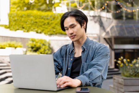 Téléchargez les photos : Portrait d'homme asiatique confiant et souriant, programmeur utilisant un ordinateur portable travaillant projet en ligne. Copywriter réussi à taper sur le clavier assis sur le lieu de travail. Technologie, entreprise prospère - en image libre de droit