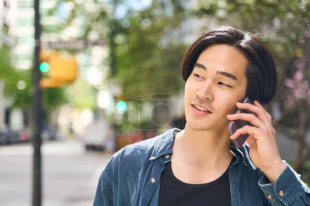 Téléchargez les photos : Portrait rapproché d'un bel homme asiatique souriant parlant sur un téléphone portable regardant loin dans la rue, copiant l'espace. Concept technologique - en image libre de droit
