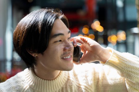 Foto de Primer plano guapo asiático hombre sosteniendo el teléfono móvil, hablando, mirando hacia otro lado. Hombre de negocios japonés al aire libre. Concepto de negocio, publicidad - Imagen libre de derechos