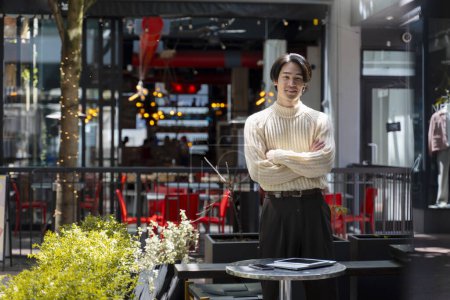 Foto de Exitoso joven empresario asiático de pie cerca del lugar de trabajo con los brazos cruzados. Empresario japonés que trabaja en línea y utiliza tecnología moderna - Imagen libre de derechos