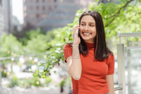 Photo for Authentic portrait of smiling beautiful Indian woman talking on mobile phone, answering call looking away standing on urban street, copy space Technology concept - Royalty Free Image