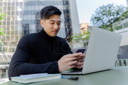 Photo for Handsome asian man holding mobile phone, text message, working on laptop, remote work outdoors. Attractive chinese male online shopping. Concept of successful developer - Royalty Free Image