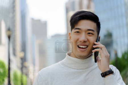 Foto de Feliz guapo asiático hombre de negocios hablando en el teléfono móvil mirando hacia la calle, espacio de copia. Negocios exitosos, concepto de tecnología - Imagen libre de derechos