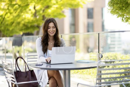 Foto de Retrato de una alegre mujer de negocios usando laptop, computadora, sentada en el lugar de trabajo. Mujer alegre y confiada escribiendo, freelancer trabajando en línea. Estudiante sonriente estudiando afuera en el parque - Imagen libre de derechos