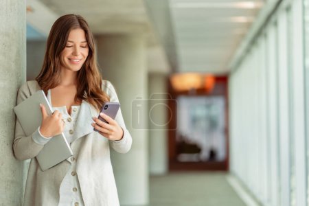Photo for Portrait of beautiful smiling woman, worker holding mobile phone, laptop working online, check email in modern office. Successful happy freelancer receive payment. Technology, mobile banking concept - Royalty Free Image