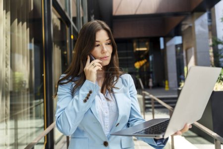 Photo for Beautiful pensive woman talking on mobile phone, using laptop, checking mail. Successful serious female secretary, worker working online looking at screen. Concept of multitasking, communication - Royalty Free Image