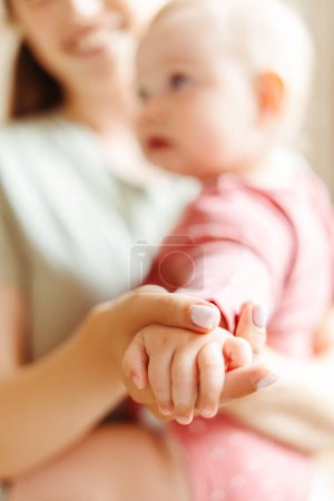 Téléchargez les photos : Attrayant, souriant femme tenant petit beau bébé, accent sélectif sur la main du bébé. Femme positive avec enfant. Amour, soins, concept de parentalité - en image libre de droit
