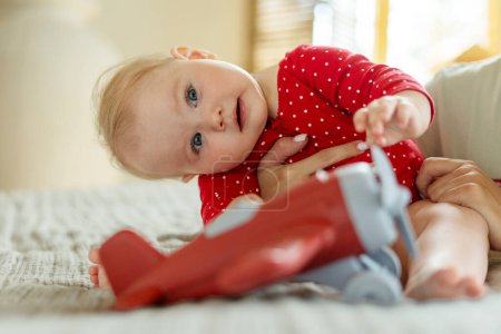 Photo for Portrait of beautiful smiling baby sitting on bed in living room at home, playing with airplane. Concept of happy childhood, child development - Royalty Free Image