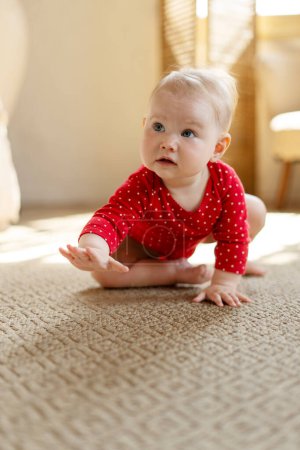 Foto de Adorable bebé lindo arrastrándose en el suelo en la sala de estar en casa. Hermosa niña creciendo. Concepto de desarrollo, infancia feliz - Imagen libre de derechos