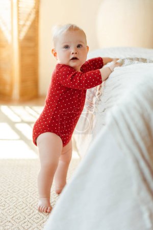 Téléchargez les photos : Portrait de mignon petit tout-petit portant des vêtements de bébé rouge marchant à la maison. Concept de la première étape - en image libre de droit