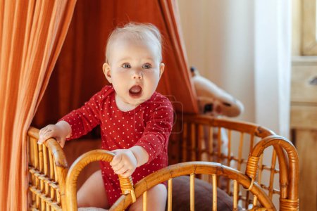 Foto de Retrato de un lindo niño pequeño con ropa roja de bebé de pie en su cama en casa. Concepto de primer paso - Imagen libre de derechos
