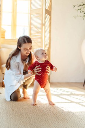 Photo for Vertical view of the young smiling mother teaching to walk her child at home. Happy family together. First step, baby development concept - Royalty Free Image