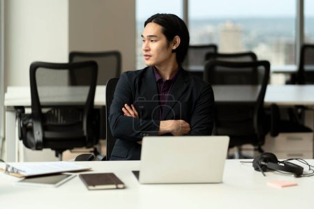 Téléchargez les photos : Portrait d'un gestionnaire asiatique sérieux, homme d'affaires prospère avec les bras croisés regardant ailleurs assis dans le bureau - en image libre de droit
