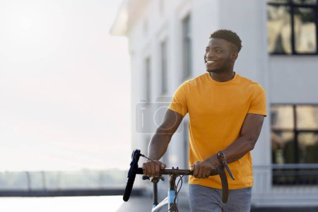 Photo for Handsome smiling african american man looking away while standing on urban street near bicycle. Young happy hipster walking outdoors. Transportation concept - Royalty Free Image