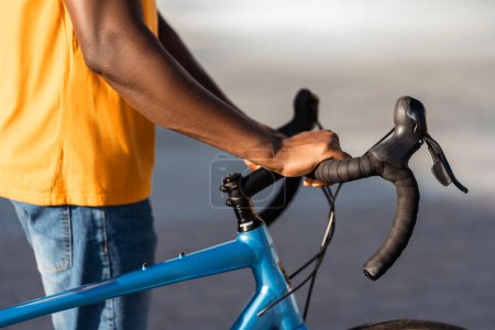 Photo for Closeup portrait of African man holding bicycle handlebars on urban street selective focus. Nigerian male rider walking outdoors. Concept of healthy lifestyle - Royalty Free Image