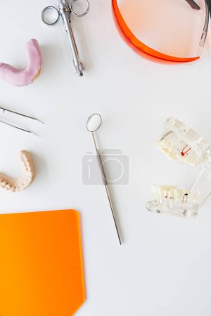 Foto de Vista superior del espejo dental, fórceps de hierro y modelos de dientes colocados sobre la mesa. Cuadro vertical de los instrumentos dentales - Imagen libre de derechos