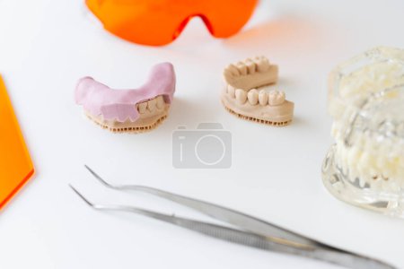 Téléchargez les photos : Mâchoires humaines en céramique. Pinces en fonte dentaire en porcelaine et fer posées à la table blanche. Orthodontie, correction des morsures. Aides visuelles dentaires - en image libre de droit