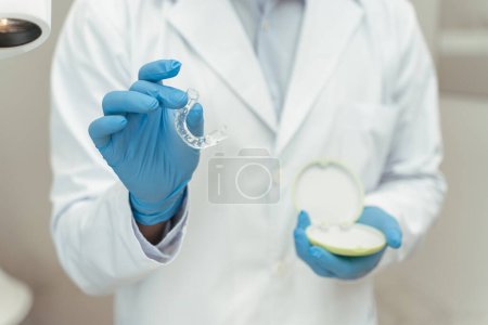 Téléchargez les photos : Médecin dentiste en gants de latex tenant des aligneurs orthodontiques, accent sélectif sur la main. Concept d'alignement des dents, soins dentaires - en image libre de droit