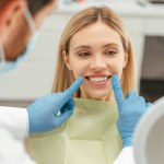 Portrait of beautiful smiling caucasian woman looking in mirror, checking her teeth in modern dental clinic. Health care concept