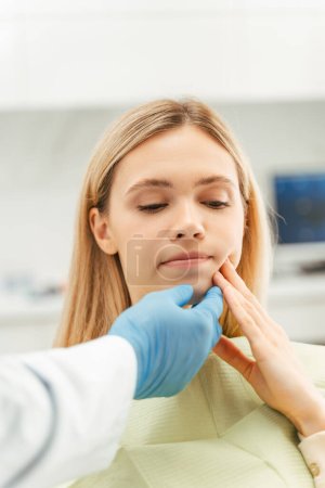 Téléchargez les photos : Patient féminin touchant la joue, ayant mal aux dents, attendant une injection d'anesthésique pour un traitement dentaire indolore en clinique dentaire. Médecin dentiste toucher son visage avec la main - en image libre de droit