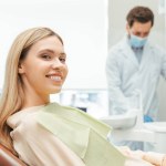 Young beautiful smiling woman, patient sitting in modern dental clinic with dentist on background. Dental treatment, health care concept 