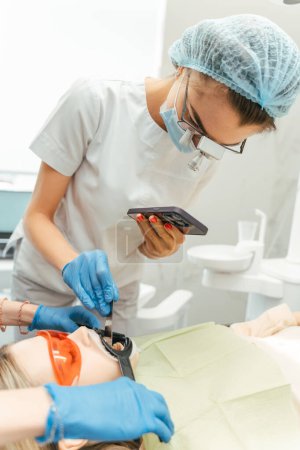 Téléchargez les photos : Dentiste femelle tenant du matériel de fer tout en vérifiant le remplissage pour la patiente en clinique dentaire. Dents concept de procédures de santé - en image libre de droit