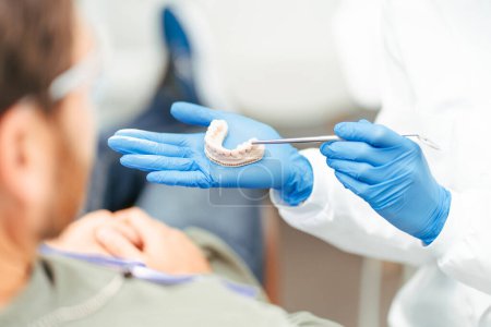 Foto de Odontólogo de cerca en guantes de látex mostrando modelo de mandíbula a paciente, enfoque selectivo. Cuidado dental, concepto de tratamiento dental - Imagen libre de derechos