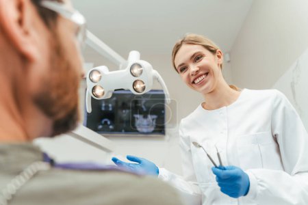 Téléchargez les photos : Portrait d'un dentiste professionnel souriant parlant avec un patient dans une clinique dentaire moderne. Soins de santé, concept d'hygiène buccale - en image libre de droit