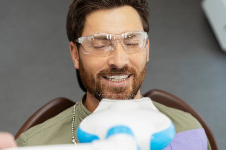 Photo for Portrait of handsome bearded man sitting in dental chair, wearing glasses with closed eyes. Visit to dentist to checking teeth. Concept treatment, whitening, dental care - Royalty Free Image