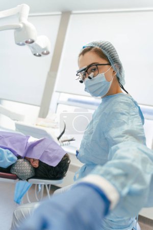 Téléchargez les photos : Chirurgiens dentaires travaillant. Dentiste professionnel avec microscope faisant un bilan dentaire sur le patient dans une clinique de chirurgie dentaire - en image libre de droit