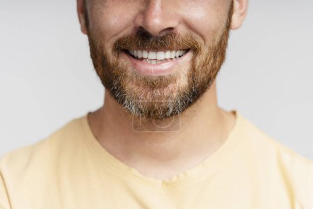 Téléchargez les photos : Portrait rapproché d'un homme barbu d'âge moyen heureux avec un sourire de dents isolé sur fond gris. Procédure dentaire, orthodontiste. Hipster confiant avec barbe élégante coupée après le service de salon de coiffure - en image libre de droit