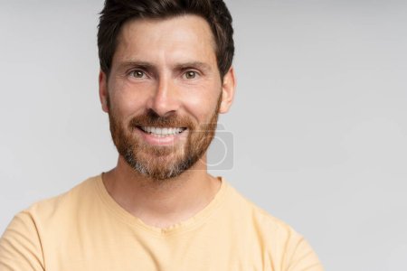 Téléchargez les photos : Portrait d'un homme barbu souriant d'âge moyen regardant une caméra isolée sur fond gris. Hipster moderne confiant avec des cheveux élégants après le service de salon de coiffure - en image libre de droit