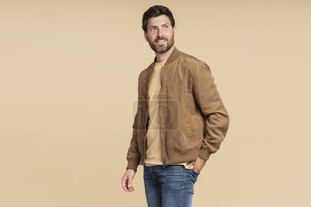 Photo for Handsome smiling bearded man wearing brown autumn jacket, stylish jeans isolated on beige background. Portrait of successful middle aged fashion model posing for pictures, studio shot - Royalty Free Image