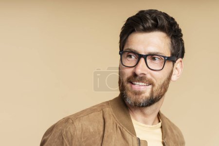 Photo for Portrait of smiling handsome bearded man wearing stylish eyeglasses looking away isolated on beige background, copy space. Vision concept - Royalty Free Image