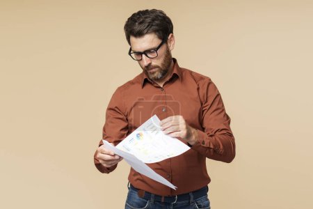 Photo for Pensive, serious, businessman wearing glasses holding business graph isolated on beige background. Male teacher working with documents - Royalty Free Image