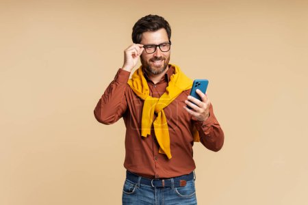 Photo for Handsome stylish smiling man holding smartphone using mobile app shopping online isolated on background. Happy hipster guy reading text message, check email. Technology, mobile banking concept - Royalty Free Image