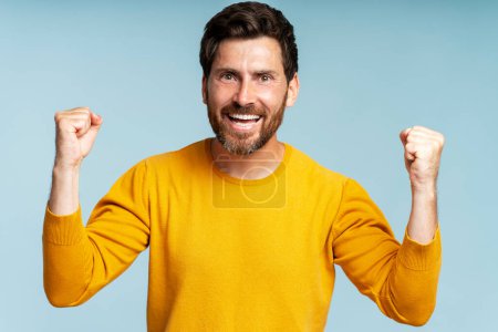 Photo for Overjoyed bearded man, winner holding arms up looking at camera, celebration success isolated on blue background. Victory concept - Royalty Free Image